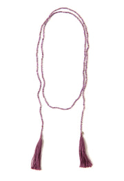 A Bohemian style Lariat Necklace, featuring 2 cotton tassels hanging from a long strand of natural, faceted amethyst stone beads, by Tribe Jewelry Designer Sarah Lewis.
