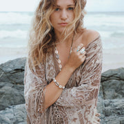 A Quartz Crystal set in engraved Sterling Silver, hangs with natural and cast Cowrie shells, and Silver beads, on a long, Bohemian Statement Necklace, handmade by Tribe Jewelry Designer Sarah Lewis. 
