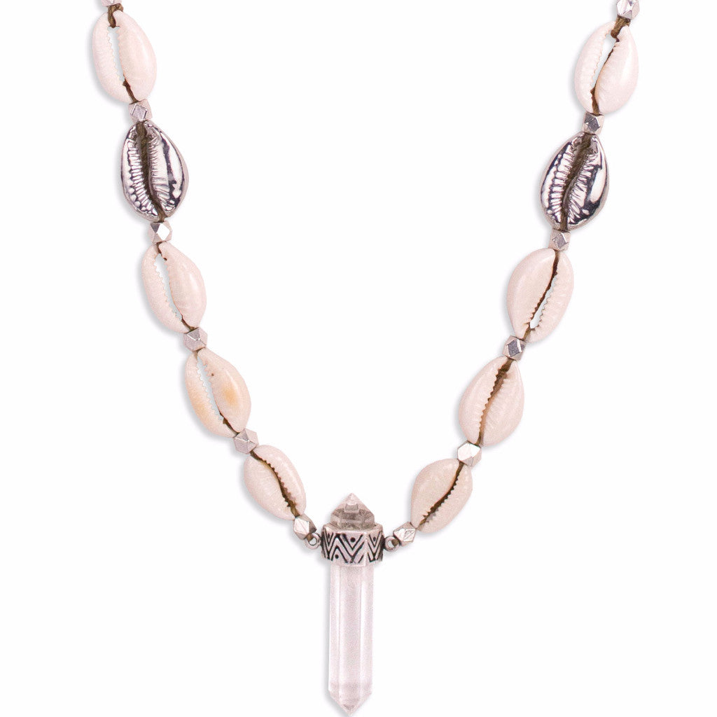 A Quartz Crystal set in engraved Sterling Silver, hangs with natural and cast Cowrie shells, and Silver beads, on a long, Bohemian Statement Necklace, handmade by Tribe Jewelry Designer Sarah Lewis. 