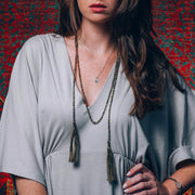 A Bohemian style Lariat Necklace, featuring 2 cotton tassels hanging from a long strand of natural, faceted labradorite stone beads, by Tribe Jewelry Designer Sarah Lewis. 