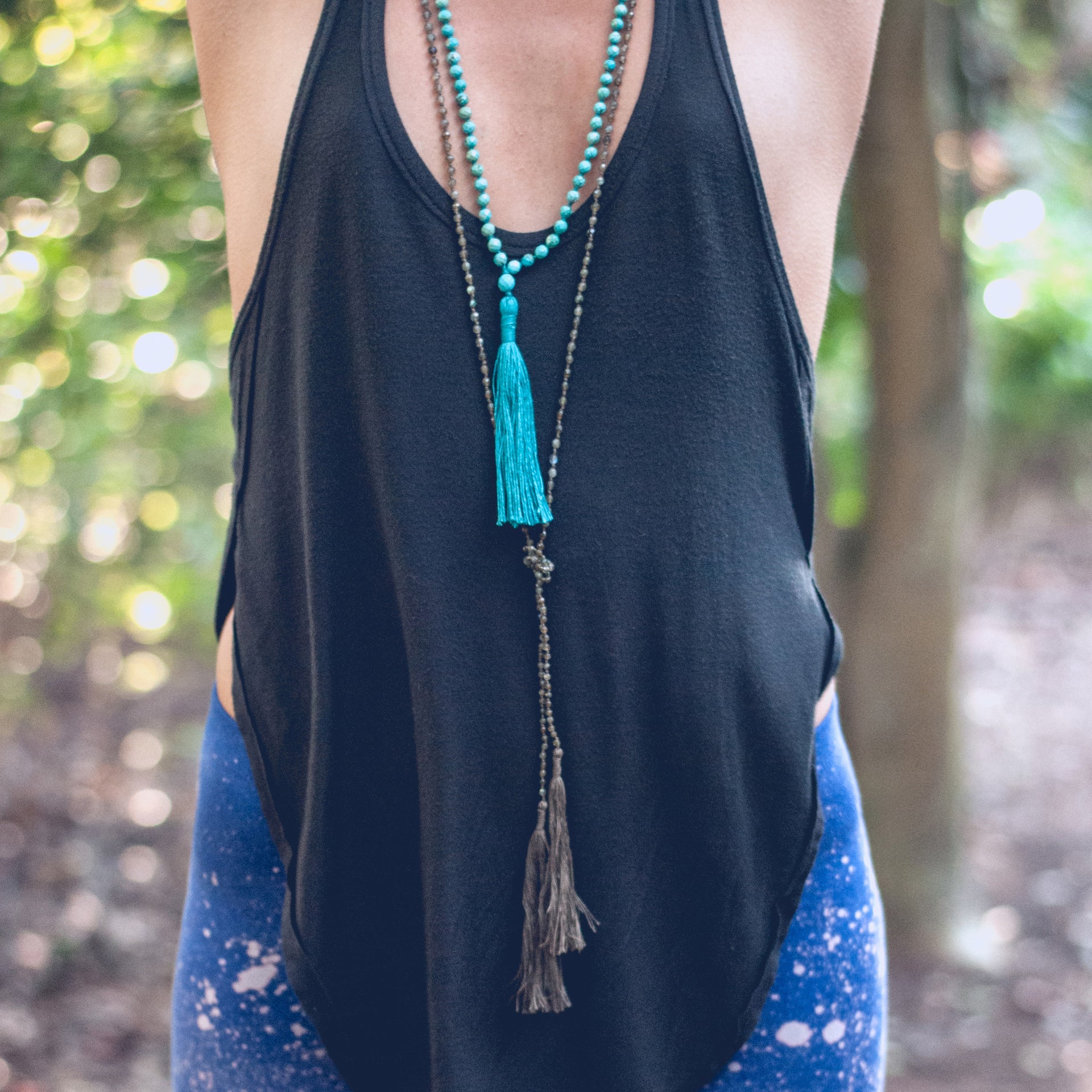 A Bohemian style Lariat Necklace, featuring 2 cotton tassels hanging from a long strand of natural, faceted labradorite stone beads, by Tribe Jewelry Designer Sarah Lewis. 