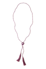 A Bohemian style Lariat Necklace, featuring 2 cotton tassels hanging from a long strand of natural, faceted amethyst stone beads, by Tribe Jewelry Designer Sarah Lewis. 