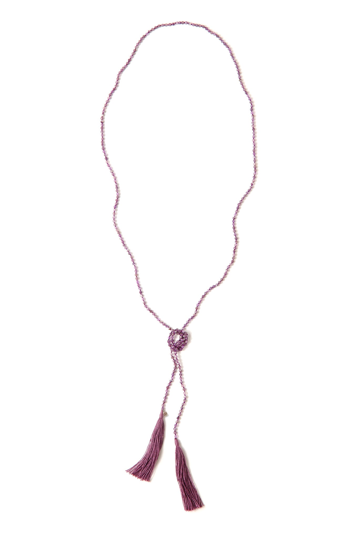 A Bohemian style Lariat Necklace, featuring 2 cotton tassels hanging from a long strand of natural, faceted amethyst stone beads, by Tribe Jewelry Designer Sarah Lewis. 