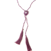 A Bohemian style Lariat Necklace, featuring 2 cotton tassels hanging from a long strand of natural, faceted amethyst stone beads, by Tribe Jewelry Designer Sarah Lewis. 