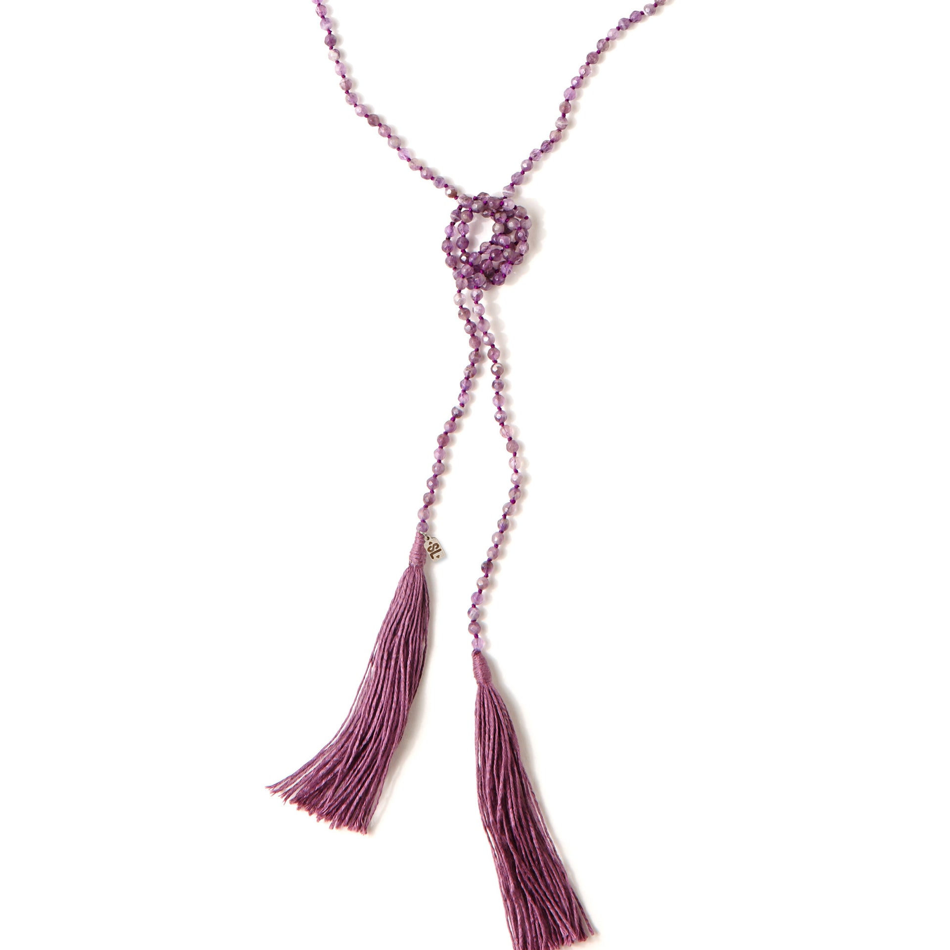 A Bohemian style Lariat Necklace, featuring 2 cotton tassels hanging from a long strand of natural, faceted amethyst stone beads, by Tribe Jewelry Designer Sarah Lewis. 
