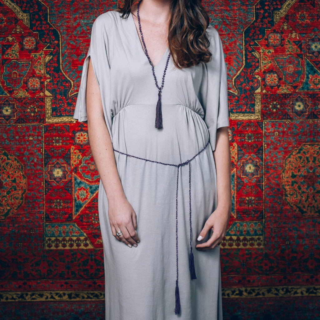 A Bohemian style Lariat Necklace, featuring 2 cotton tassels hanging from a long strand of natural, faceted amethyst stone beads, by Tribe Jewelry Designer Sarah Lewis. 