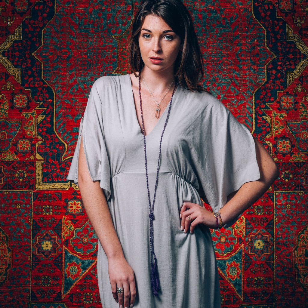 A Bohemian style Lariat Necklace, featuring 2 cotton tassels hanging from a long strand of natural, faceted amethyst stone beads, by Tribe Jewelry Designer Sarah Lewis. 