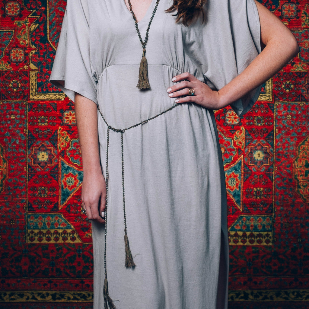 A Bohemian style Lariat Necklace, featuring 2 cotton tassels hanging from a long strand of natural, faceted labradorite stone beads, by Tribe Jewelry Designer Sarah Lewis. 