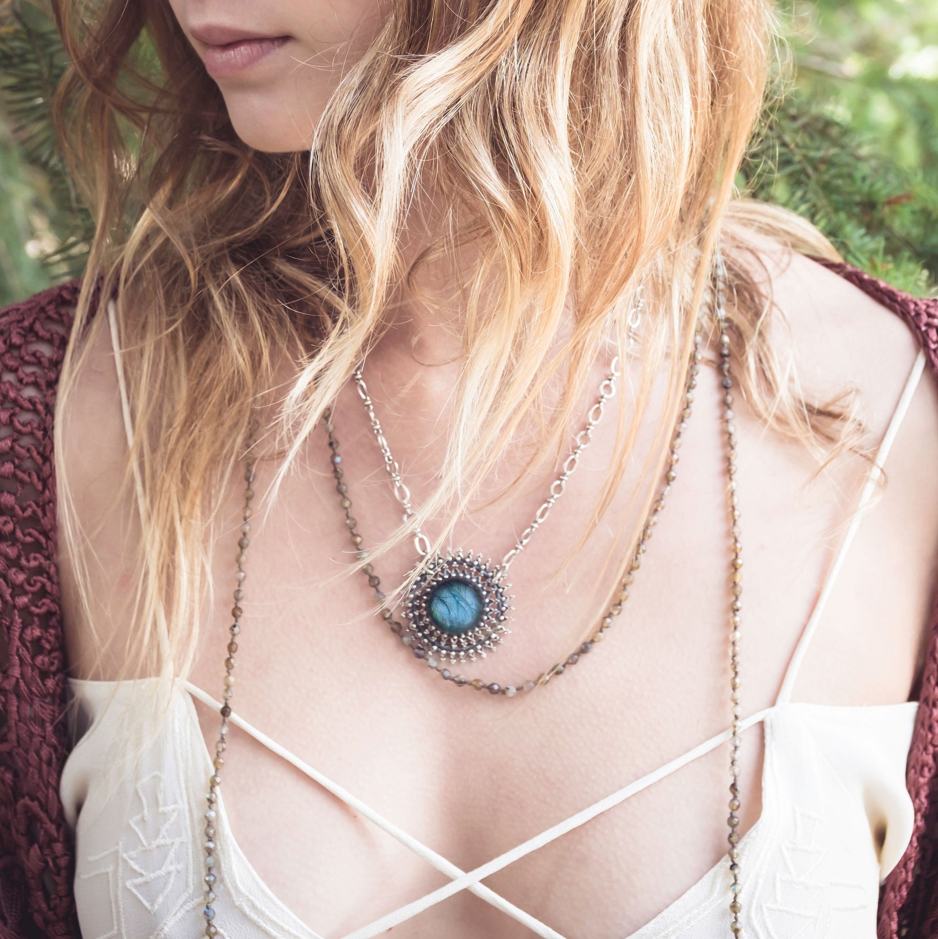 A Bohemian style Lariat Necklace, featuring 2 cotton tassels hanging from a long strand of natural, faceted labradorite stone beads, by Tribe Jewelry Designer Sarah Lewis. 