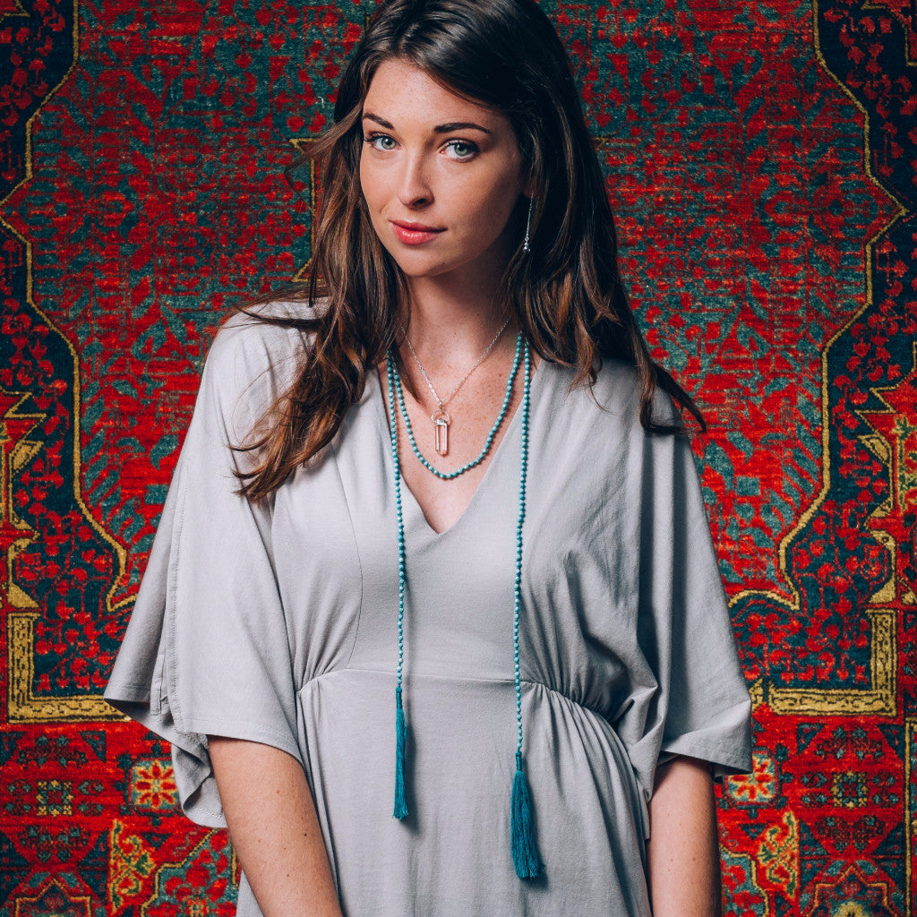 A Bohemian style Lariat Necklace, featuring 2 tassels hanging from a long strand of natural, faceted turquoise stone beads, by Tribe Jewelry Designer Sarah Lewis. 